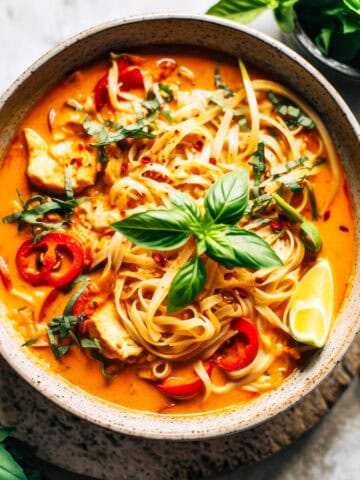 Red Curry Thai noodles with chicken and basil in a white bowl.