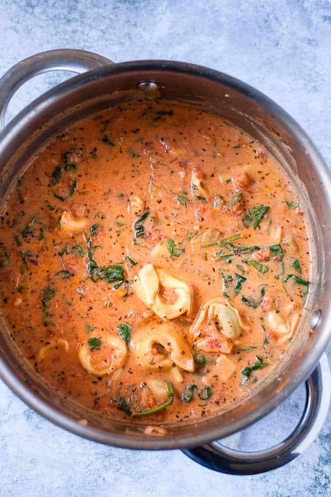 A pot of vegetable soup with tortellini on a blue table.