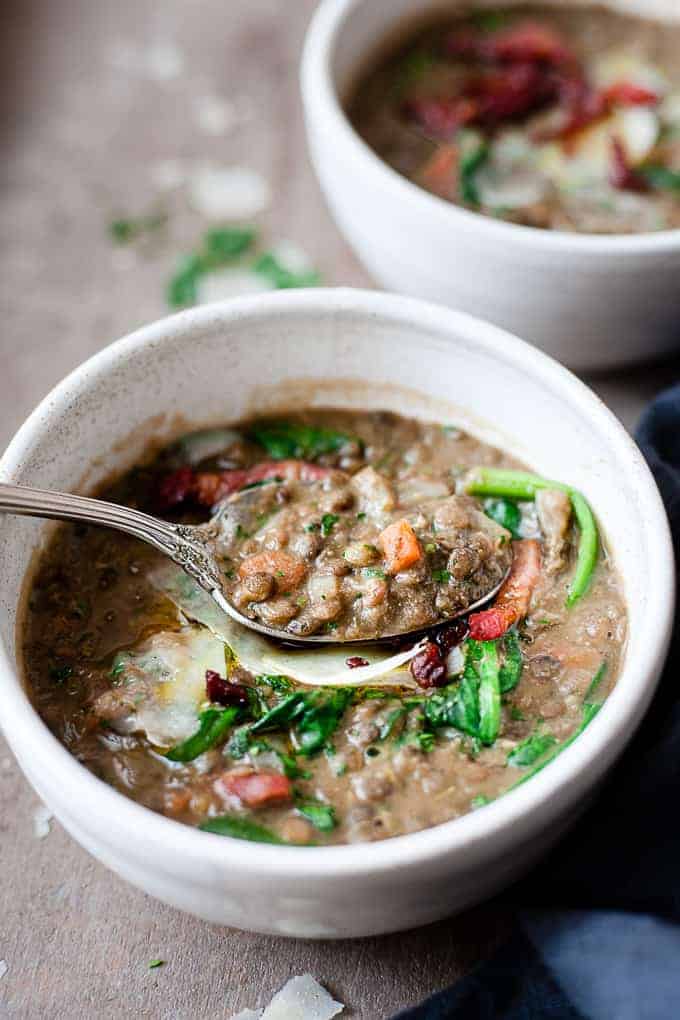 Lentil soup in a white bowl with bacon and spinach.