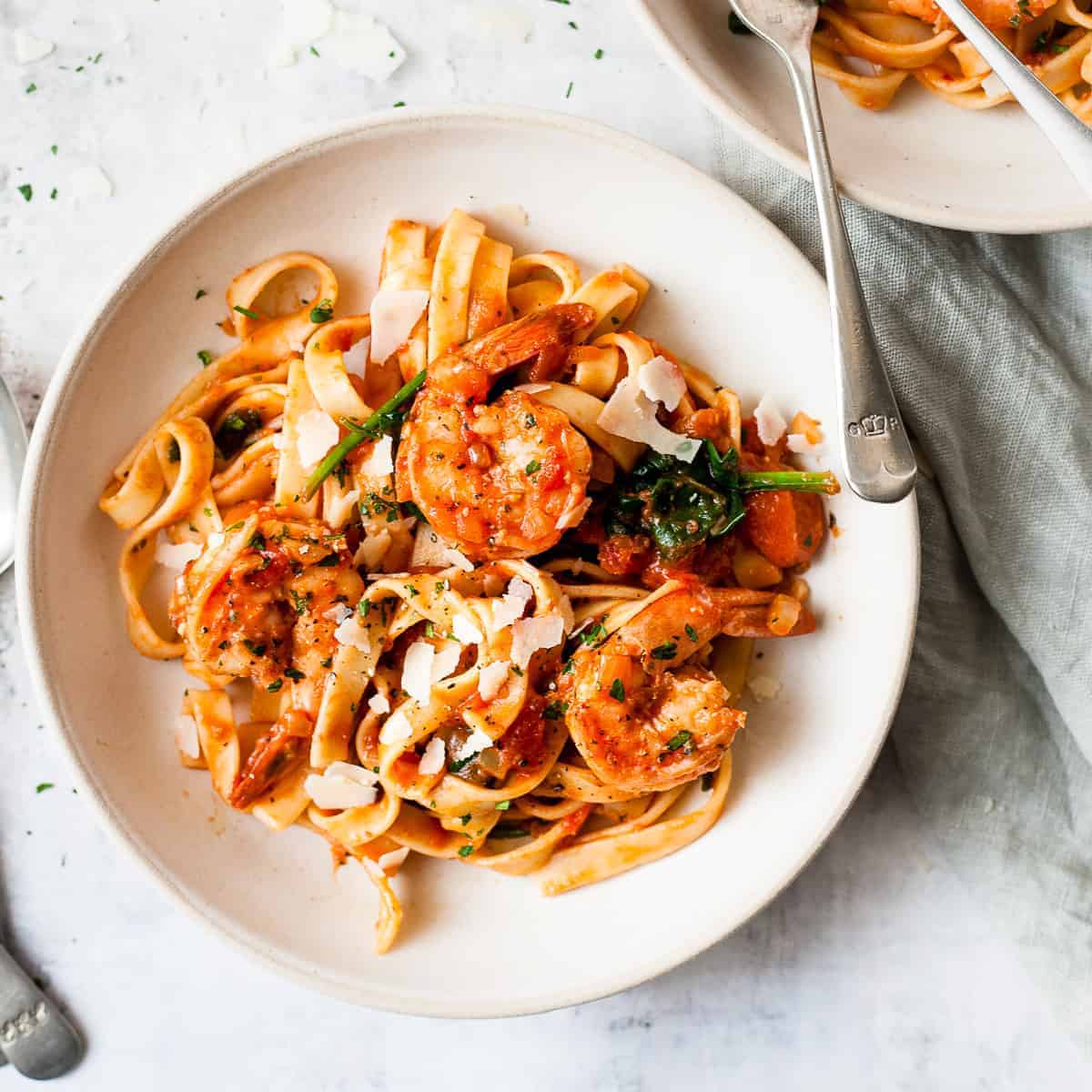Prawn pasta in a white bowl with spinach and tomato sauce.