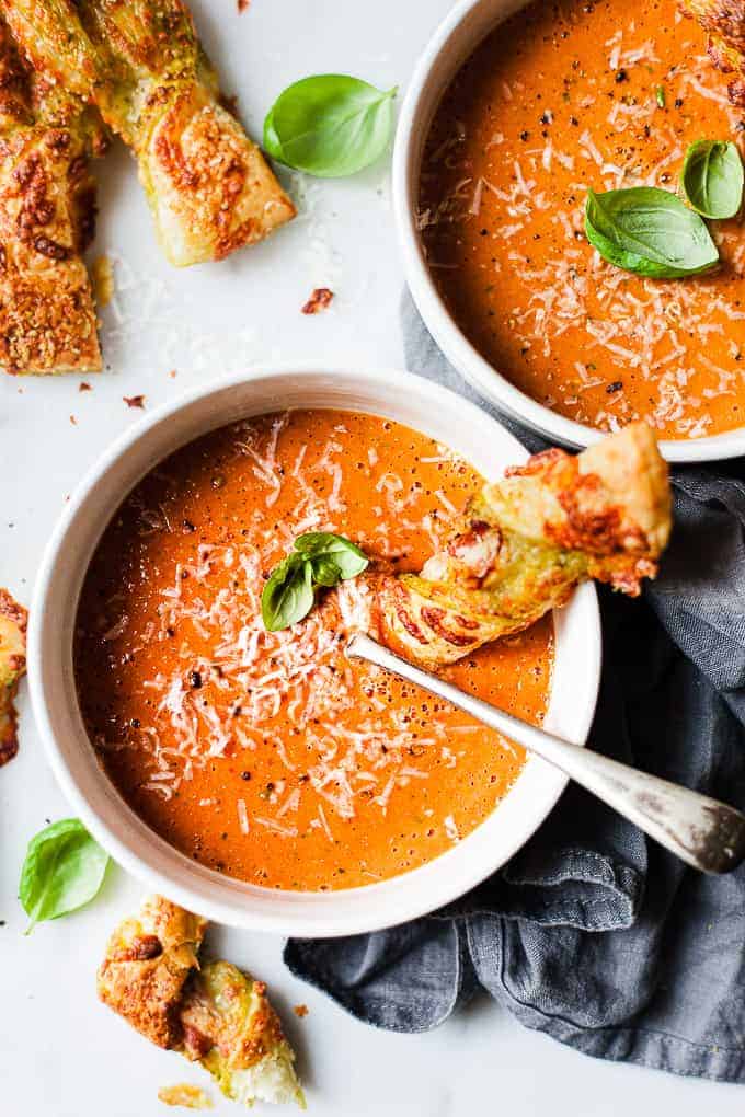 Bowl of roasted tomato soup in a white bowl with cheese breads.