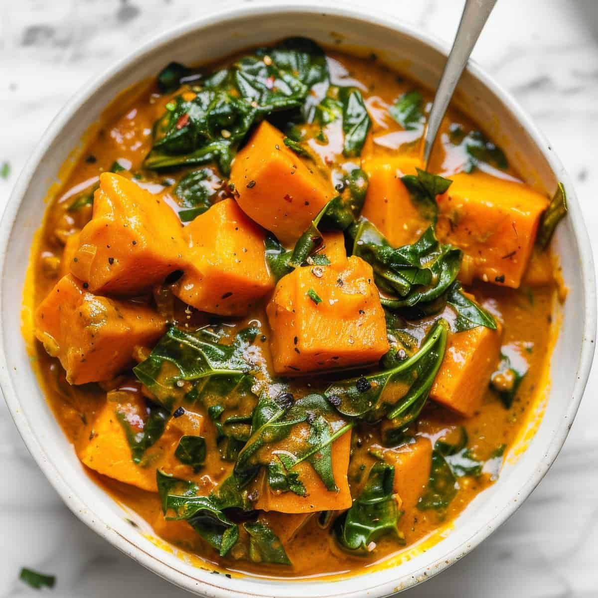 Sweet potato curry with spinach in a white bowl.