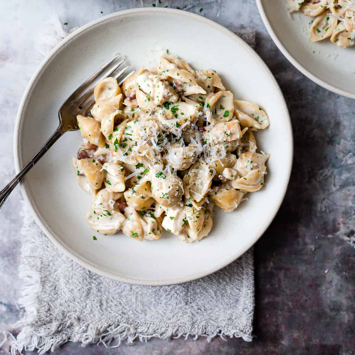 creamy chicken and bacon pasta in a white bowl on a blue table.