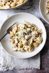 Chicken and bacon pasta in a white bowl on a blue table.