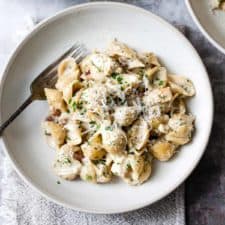Chicken and bacon pasta in a white bowl on a blue table.