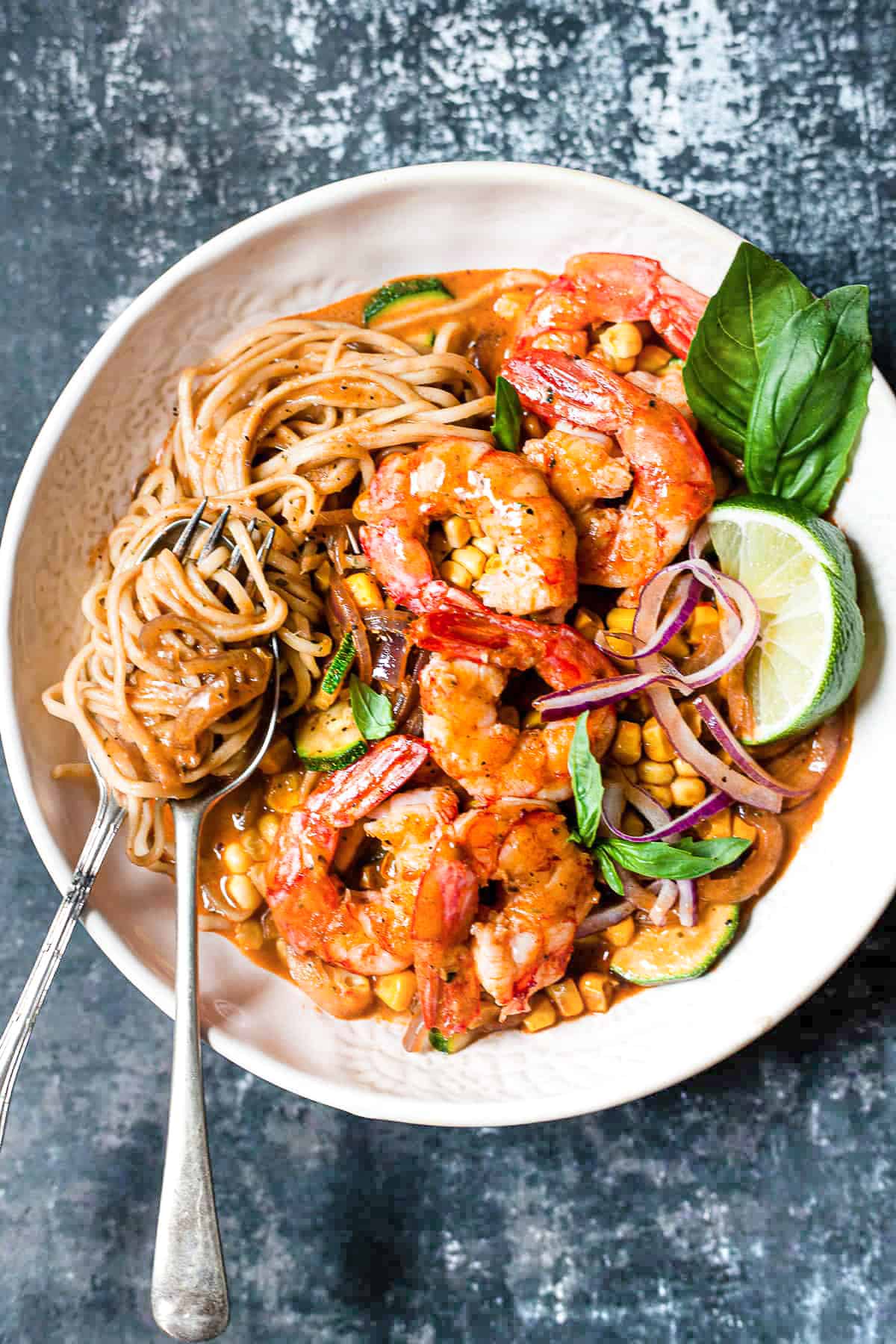 Red Thai prawn curry with noodles and vegetables in a bowl.