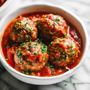 Homemade Italian style meatballs in a rustic tomato sauce in a white bowl.