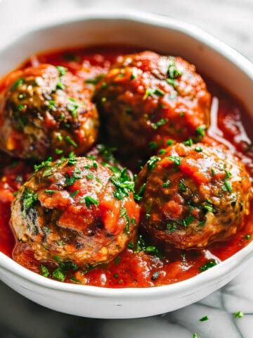 Homemade Italian style meatballs in a rustic tomato sauce in a white bowl.