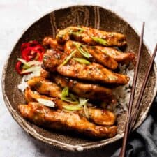 Honey chilli chicken in a brown bowl with chop sticks.