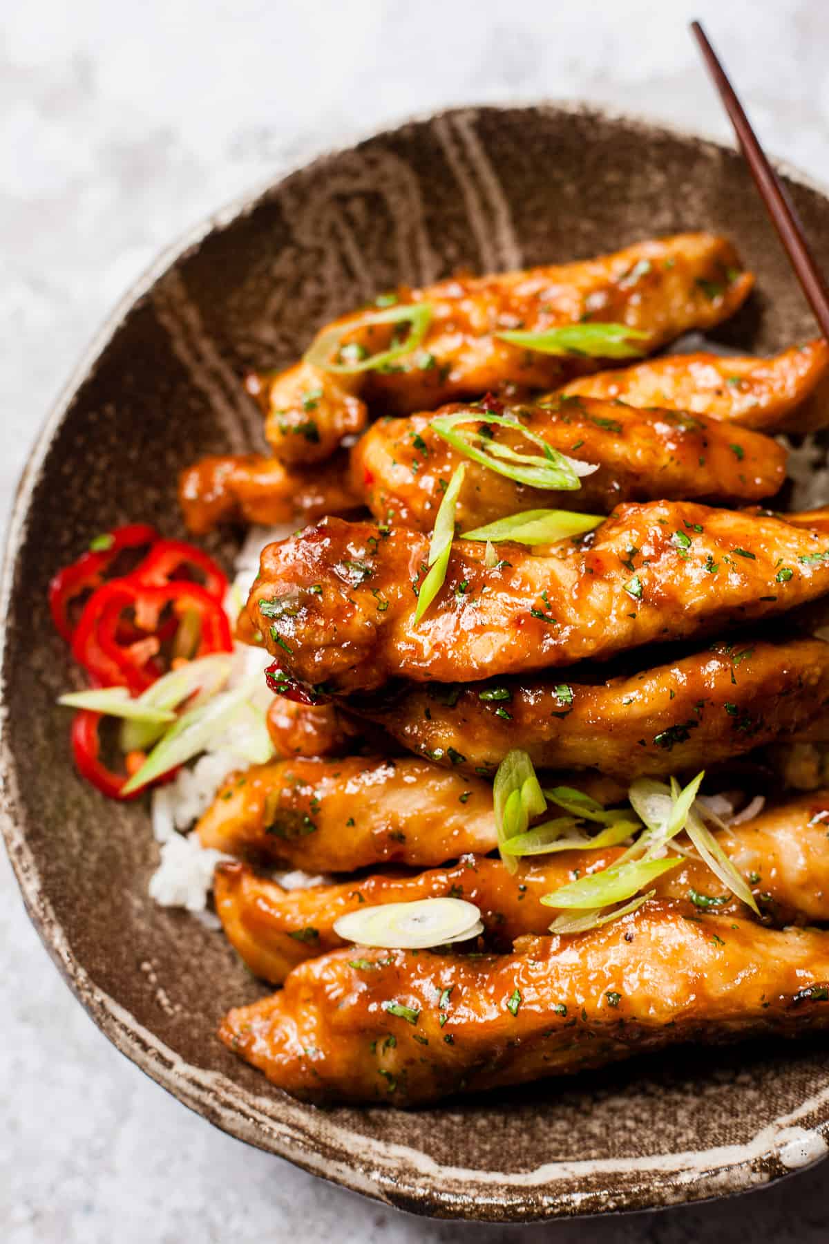 Honey chilli chicken in a brown bowl with chop sticks.