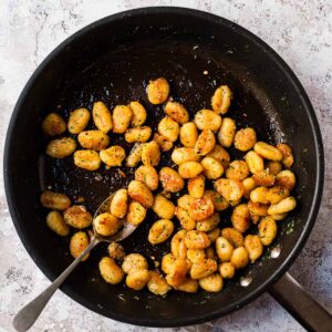 Pan fried gnocchi in a skillet with herbs and parmesan.