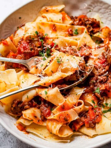 Slow cooker beef bolognese pasta in a white bowl with parsley.