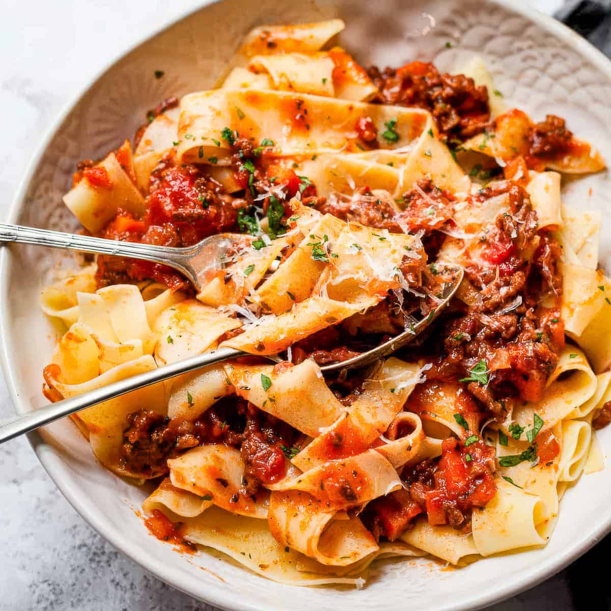 Slow cooker beef bolognese pasta in a white bowl with parsley.