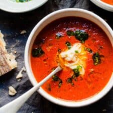 red pepper soup in a white bowl with cheese and bread.