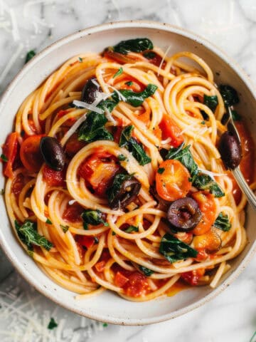 Easy anchovy tomato pasta puttanesca style in a white bowl with olives and herbs.