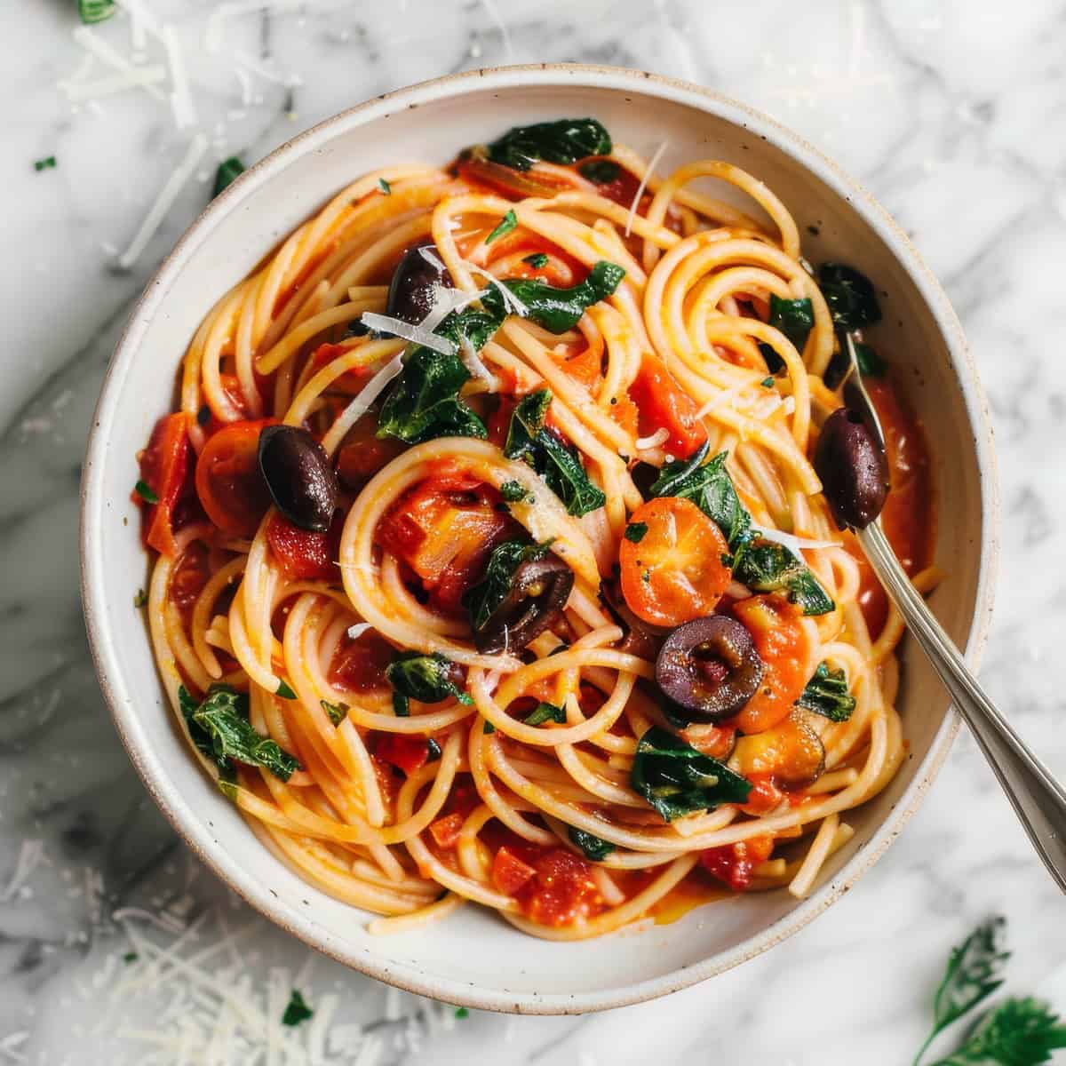 Easy anchovy tomato pasta puttanesca style in a white bowl with olives and herbs.