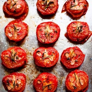 Roasted tomatoes on a baking tray with garlic and rosemary.