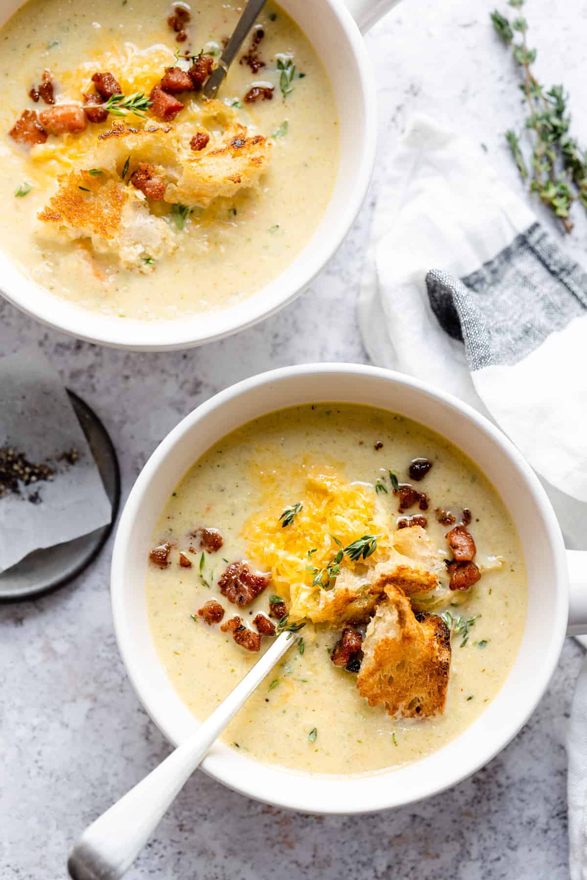 two bowls of cauliflower soup with cheese on a white table.