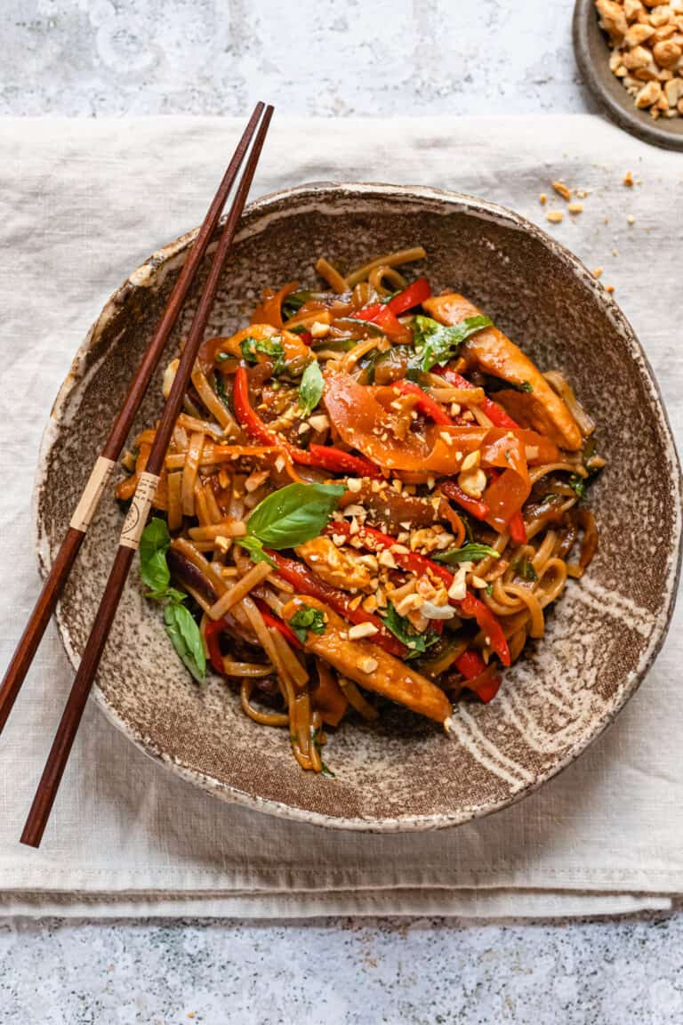 Drunken noodles on a white table with chop sticks.