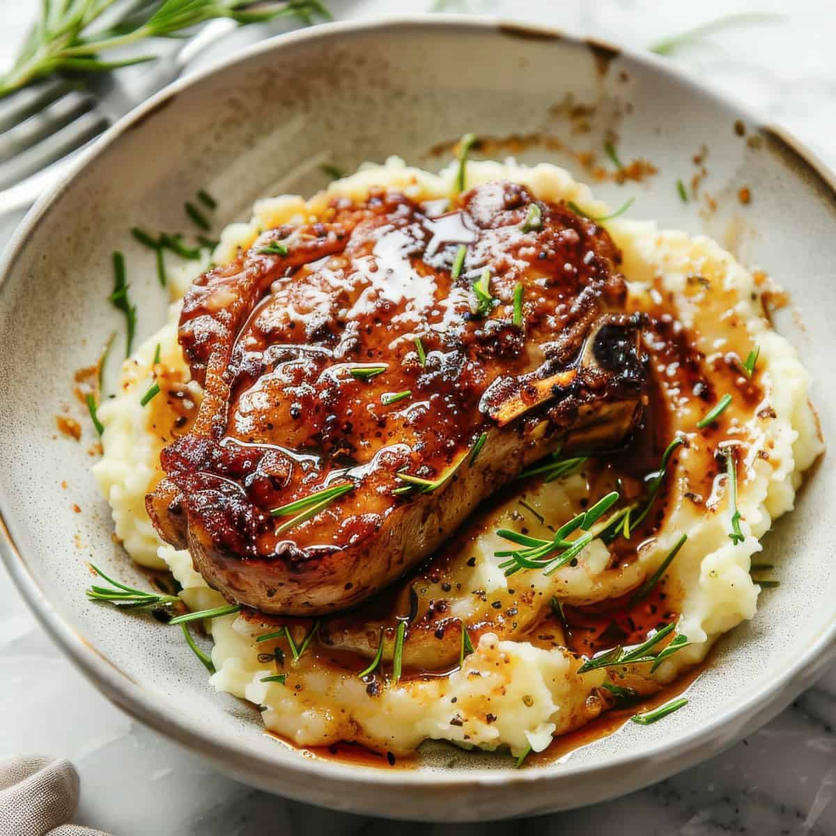 Easy brown sugar-glazed pork chops with mashed potatoes in a white bowl.