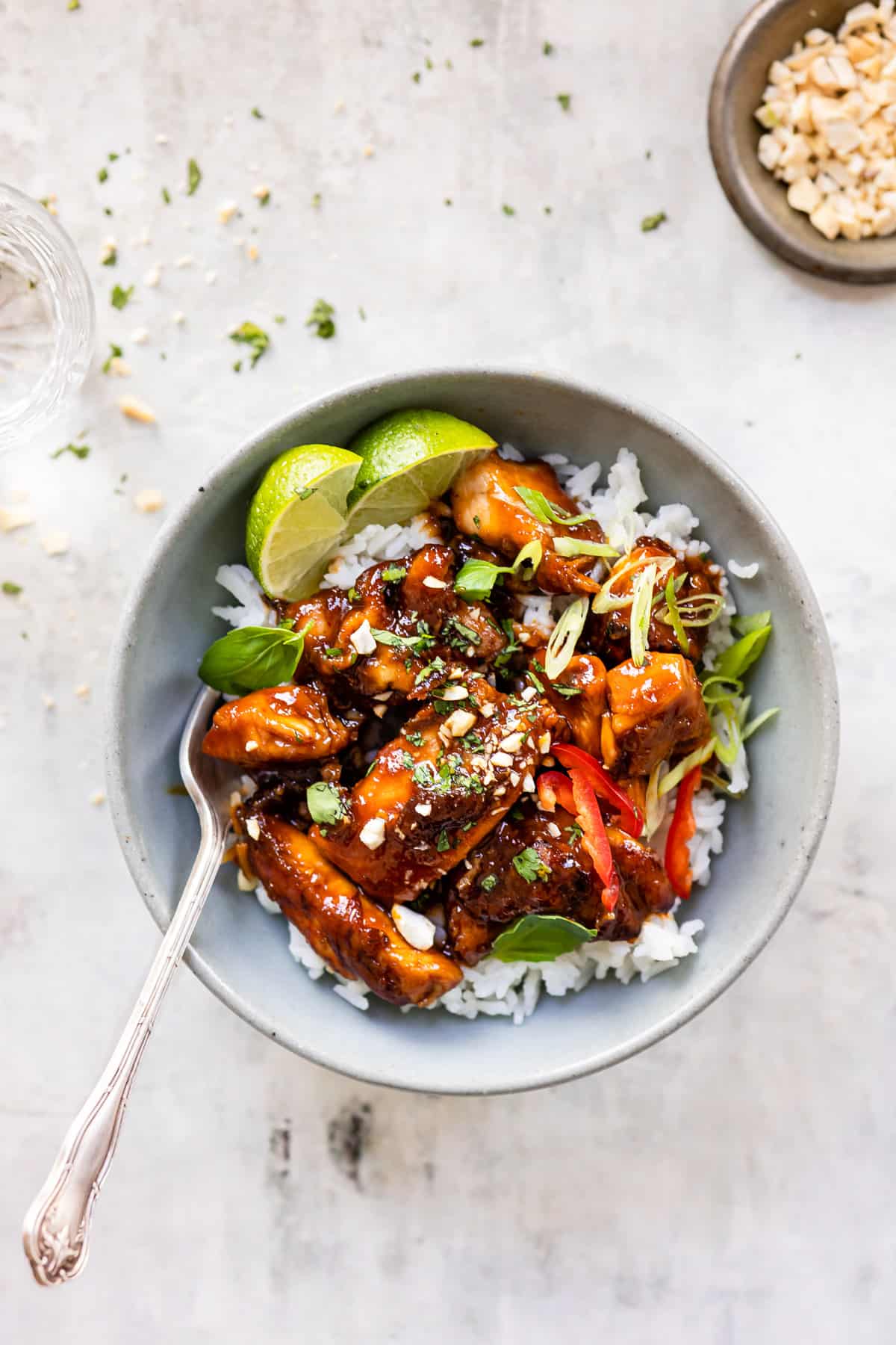 Crispy chilli chicken on a bed of rice with limes and chopped peanuts.