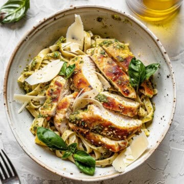 Pesto chicken pasta with parmesan cheese and basil in a bowl.