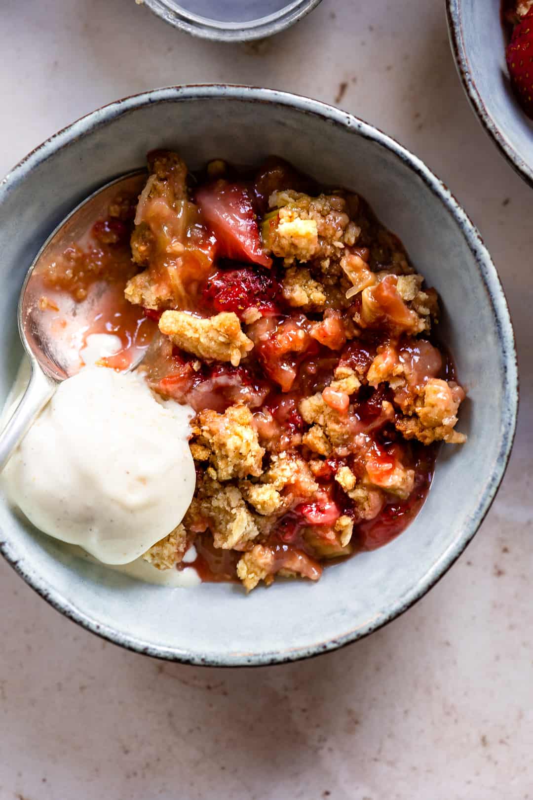 Rhubarb and strawberry crumble in a bowl with ice cream.