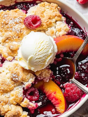 Peach and raspberry cobbler in a blue bowl with ice cream.