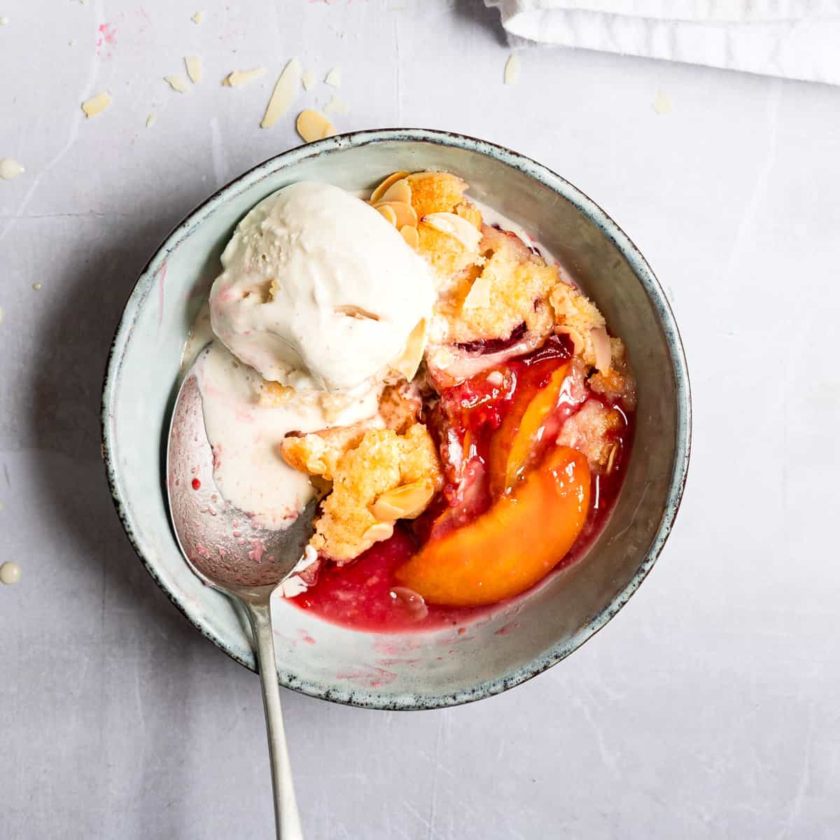 Peach and raspberry cobbler in a blue bowl with ice cream