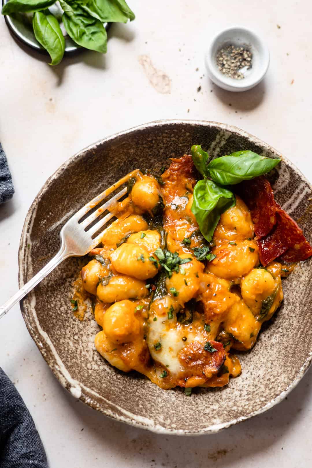 A bowl with baked gnocchi and mozzarella on a table.