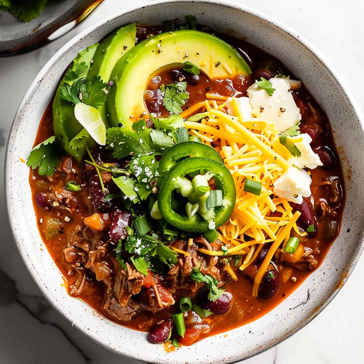 Beef chilli in a bowl with cheese, avocado and coriander.