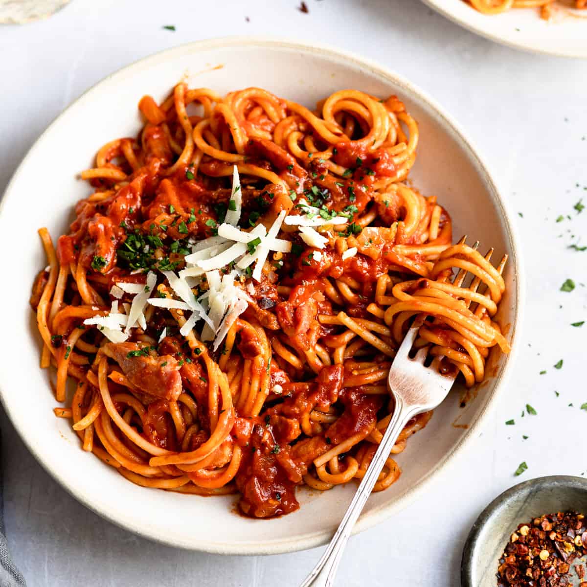 Pasta Amatriciana- Bacon tomato pasta in a white bowl with a fork.