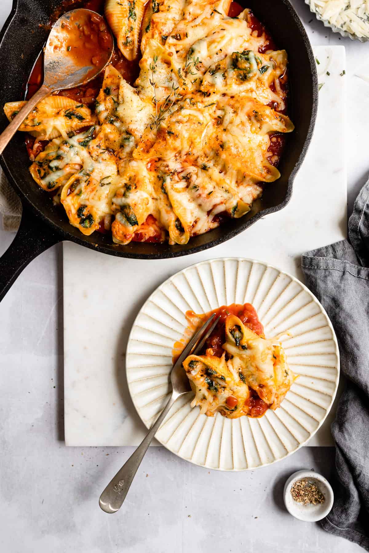 Stuffed shells in a skillet with a white plate.