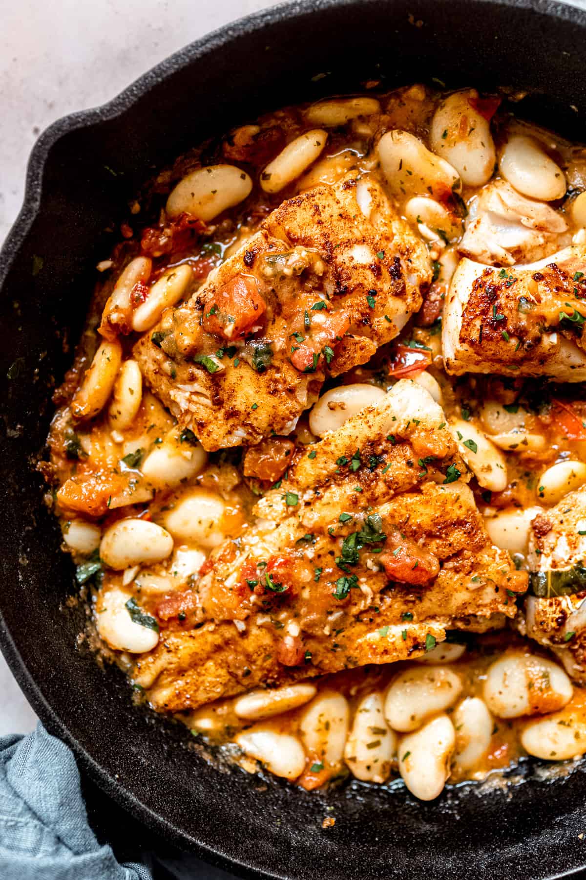 blackened cod with tomatoes and white beans in a skillet.
