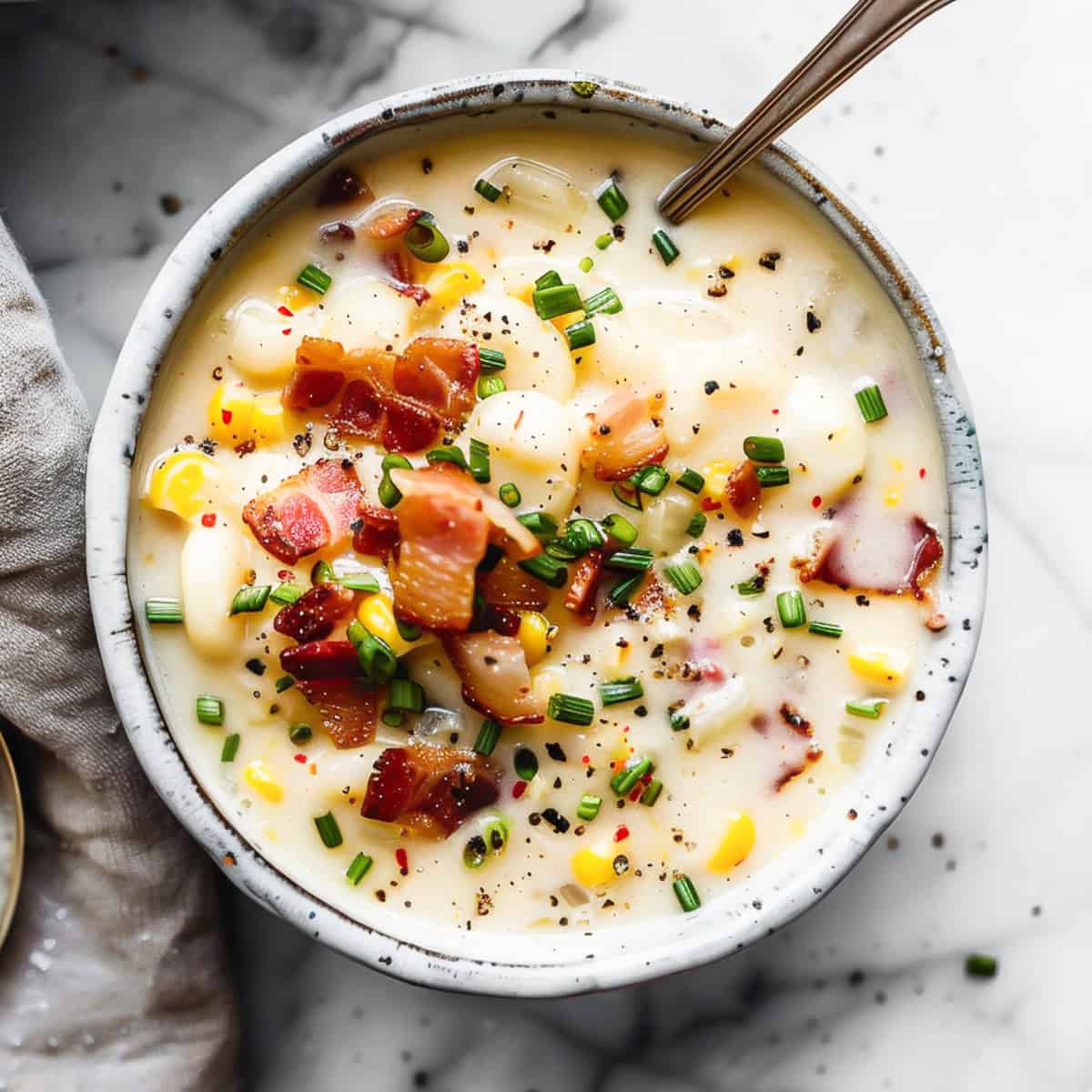 Sweetcorn chowder with bacon in a white bowl with herbs.