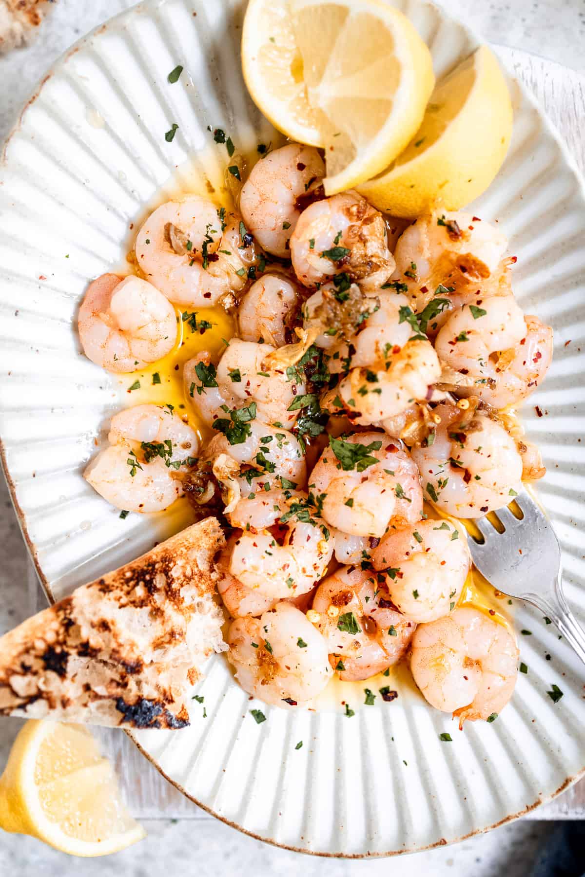 Spanish garlic prawns on a white plate with chillis and lemon.