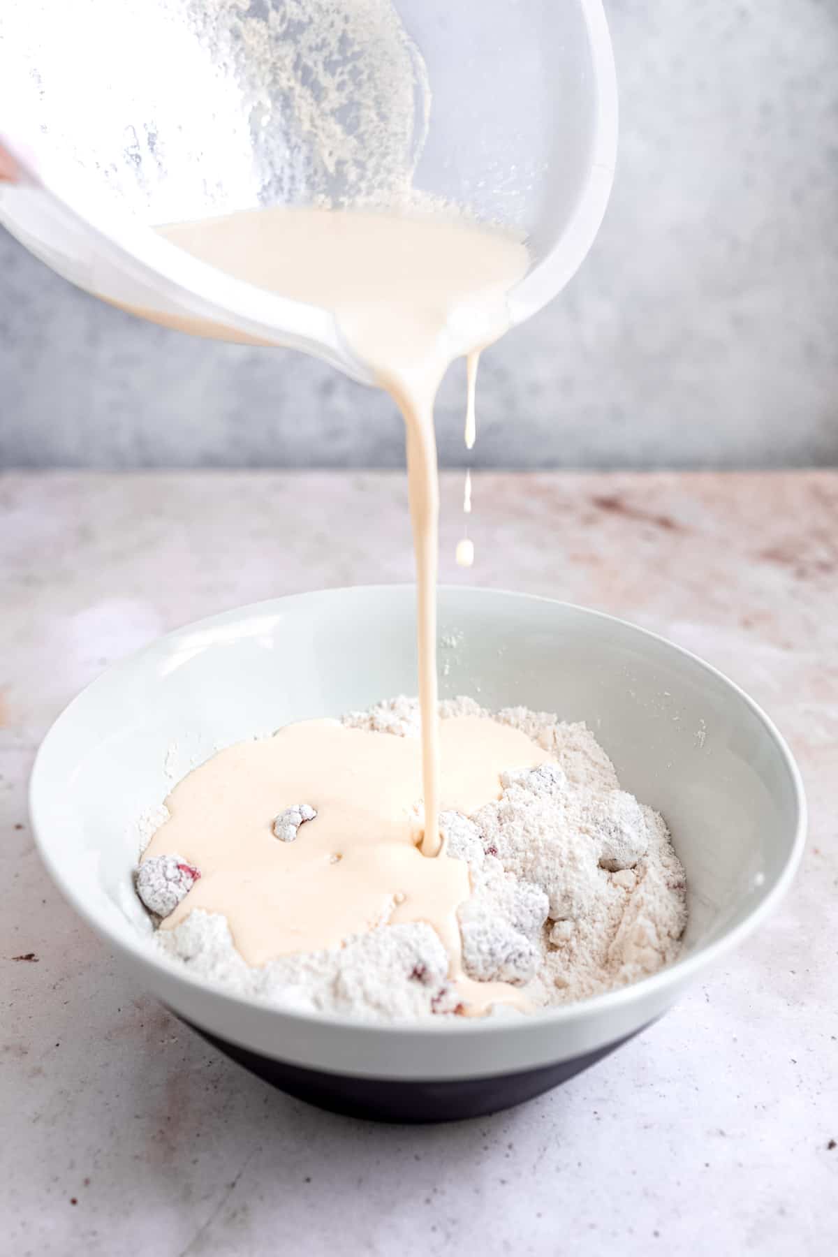 pouring the wet ingredients into the bowl with the dry ingredients and raspberries.