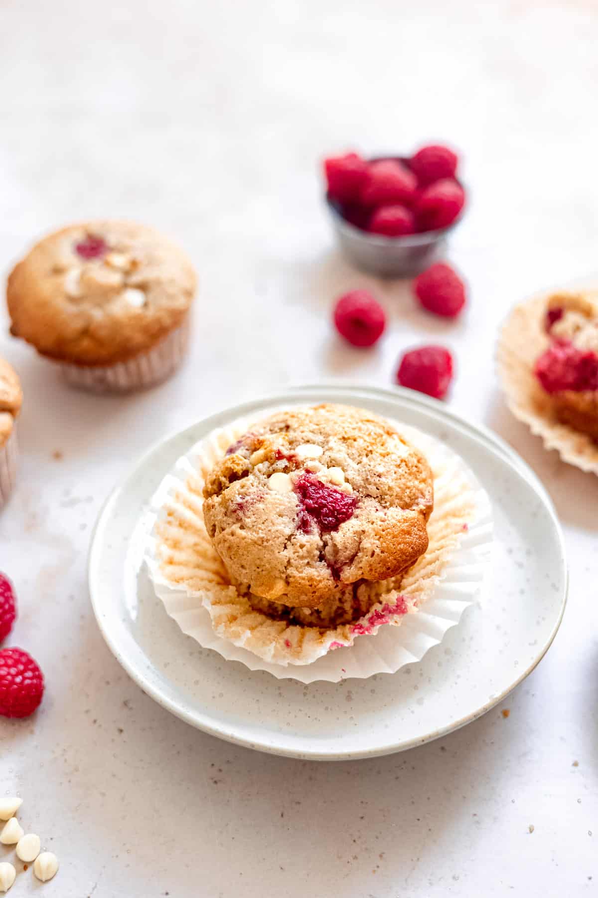 A single white chocolate and raspberry muffin on a white plate.