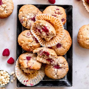 White chocolate muffins with raspberries on a baking tray.