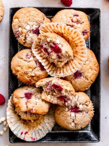 White chocolate muffins with raspberries on a baking tray.
