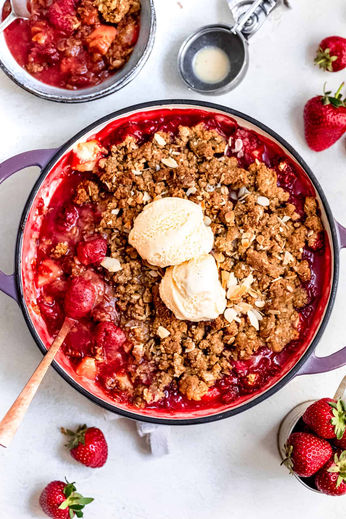 Strawberry and apple crisp with vanilla ice cream on a white table.