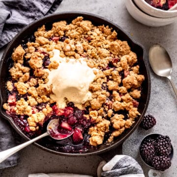 Apple and blackberry crumble in a skillet with ice cream.