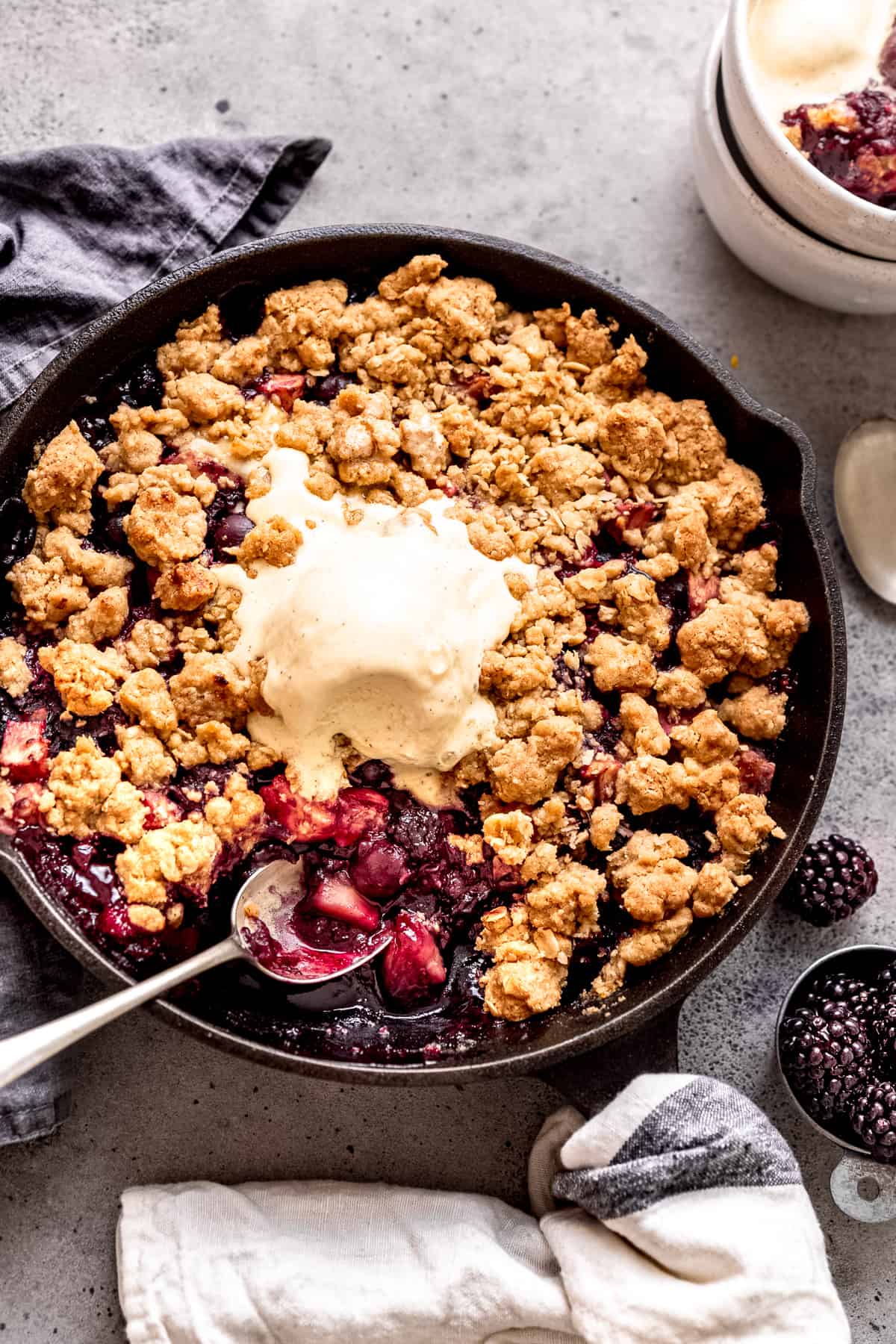 Apple and blackberry crumble in a skillet with ice cream.