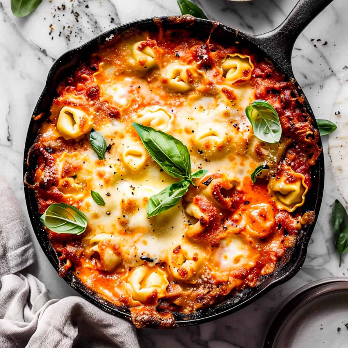 Cheesy tortellini pasta bake with basil leaves in a skillet.