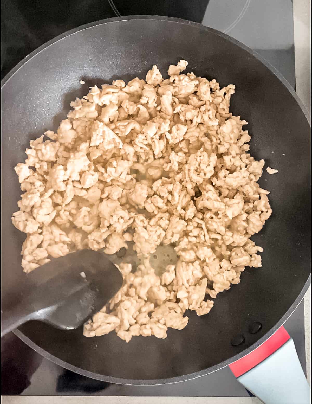 Breaking up larger chunks of turkey mince in a pan.