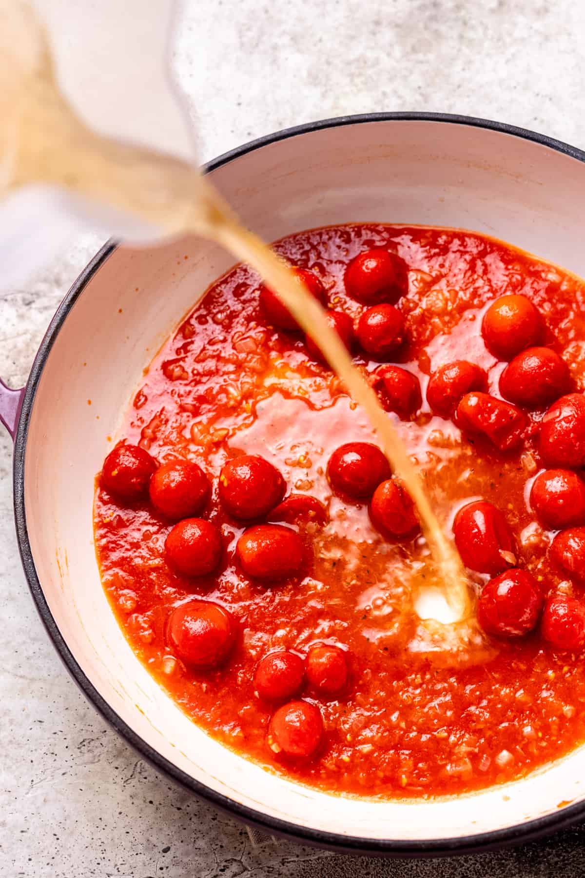 Stock being poured into a pan of tomato sauce.