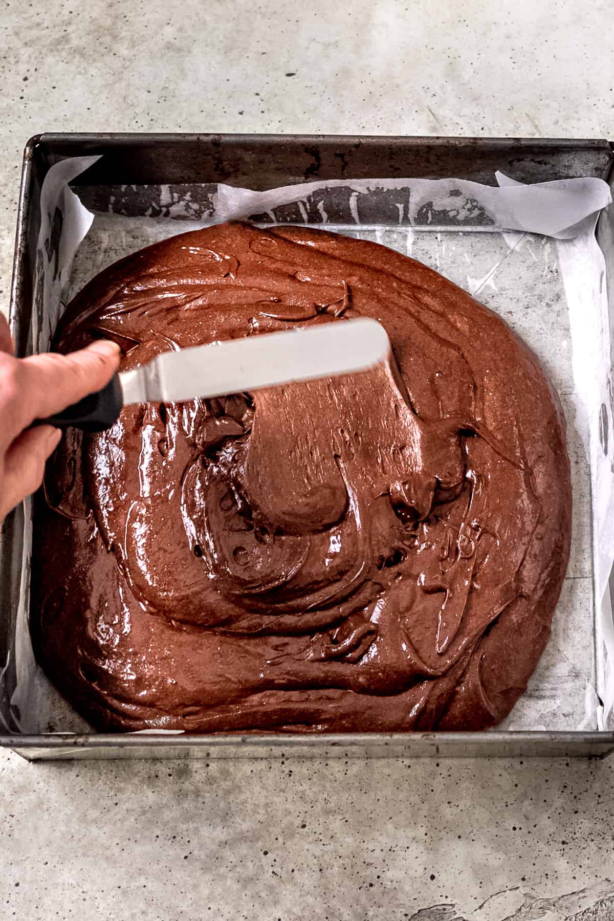 Spreading brownie batter into the lined baking tray.