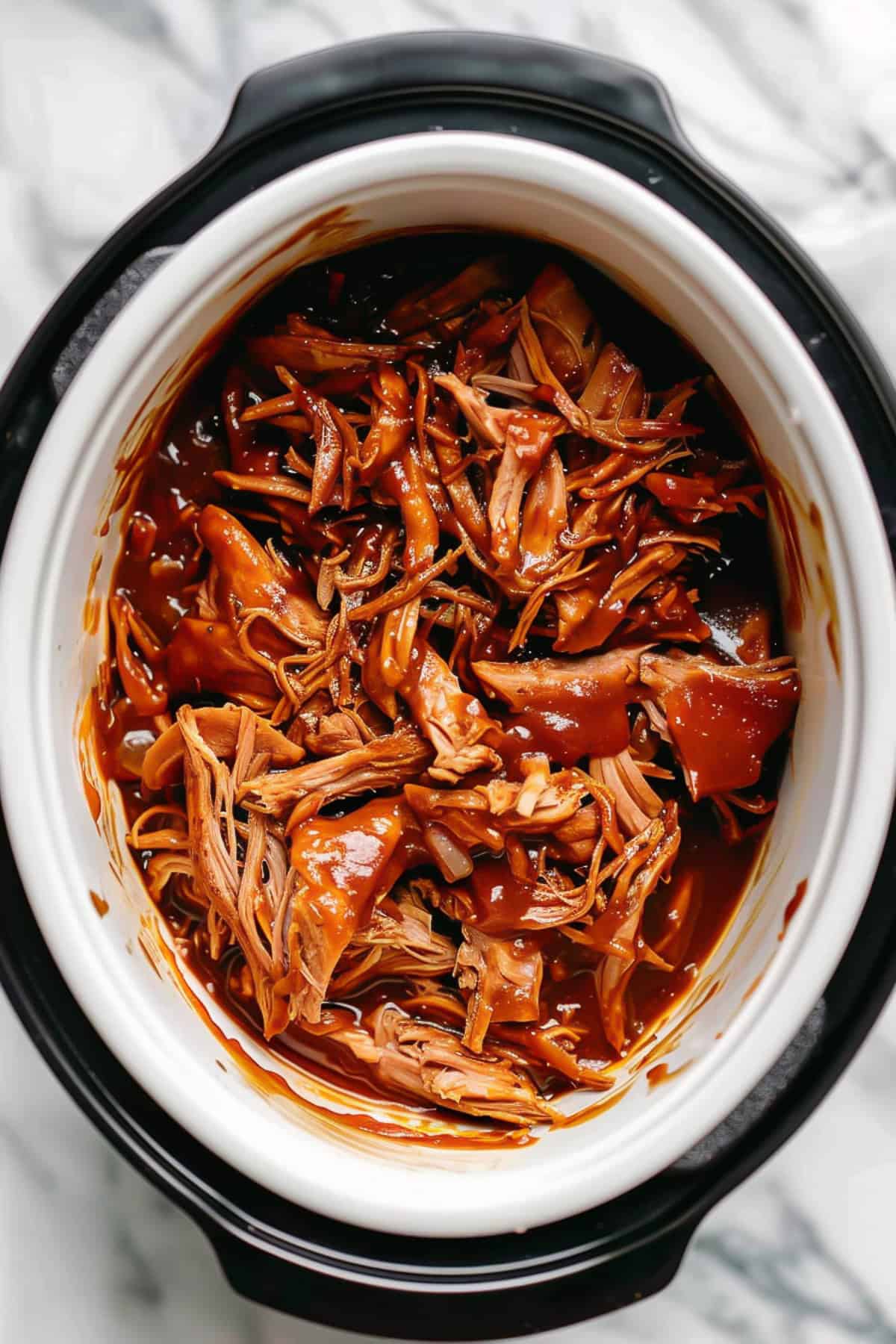 BBQ pulled chicken in a slow cooker with sauce.