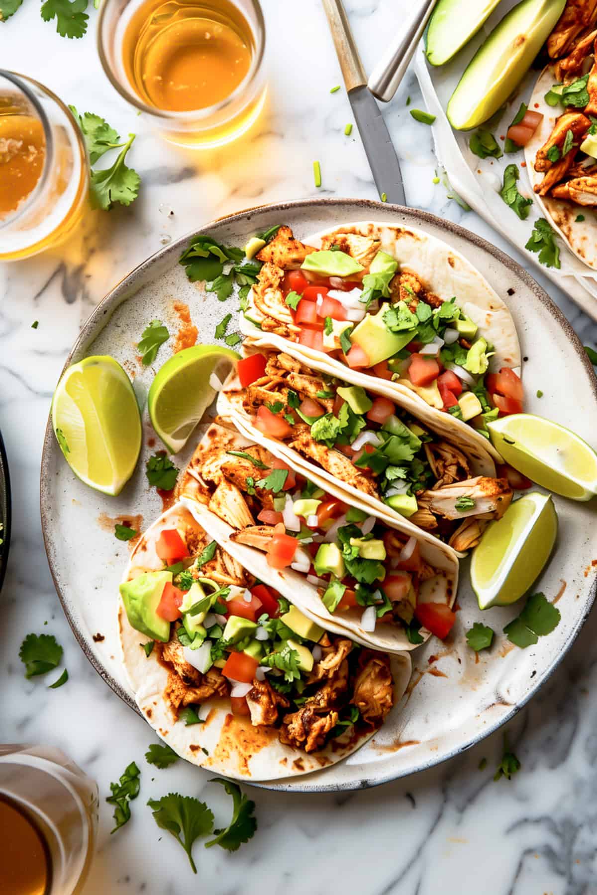 Pulled chicken tacos in tortillas with chopped tomatoes and avocado on a white plate.