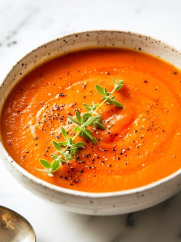 Roasted tomato soup in a bowl with thyme and olive oil.